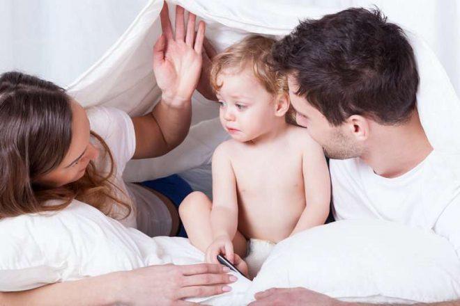 Loving parents with sad baby in bed